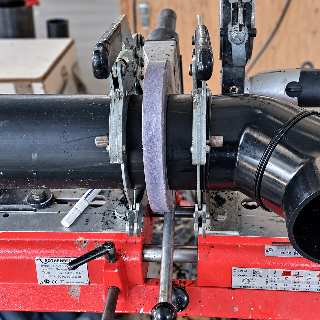 Schwarzes Kunststoffrohr in einer roten Rohrschweißmaschine